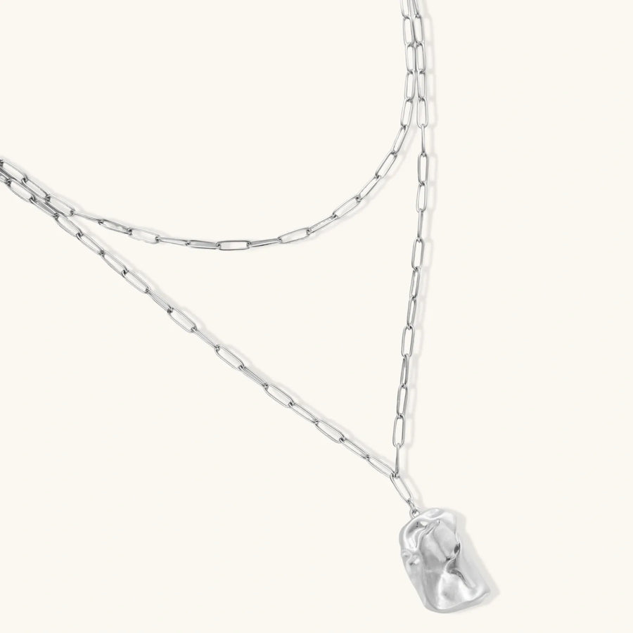 Silver layered necklace with organic flowing pendant in eco-zinc alloy on neutral background, showing adjustable chain design.