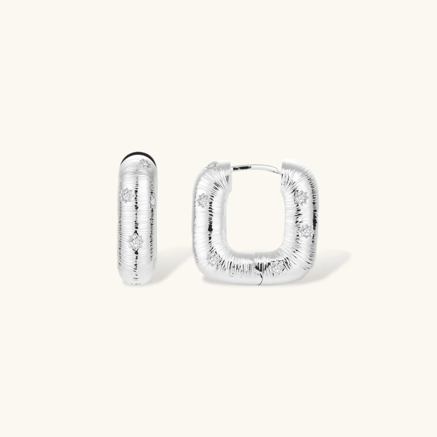 Close-up of ridged silver-plated hoop earrings with embedded crystal details on white background.