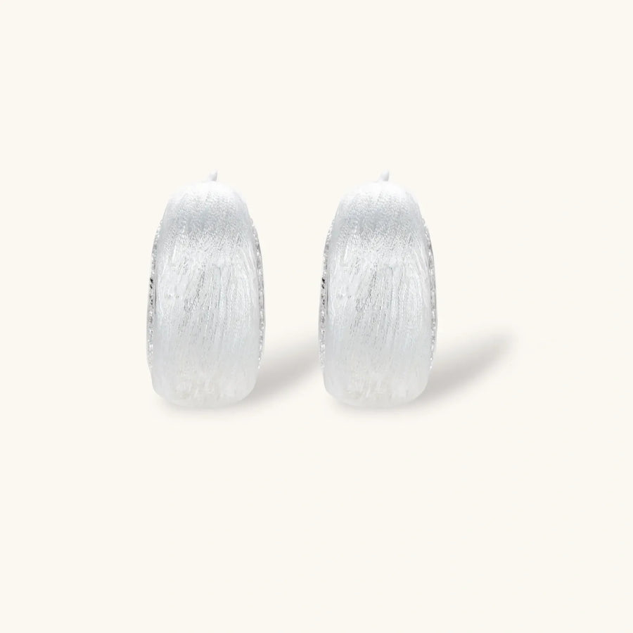 Close-up of small silver-plated hoop earrings with brushed texture and a row of sparkling zircon crystals on white background