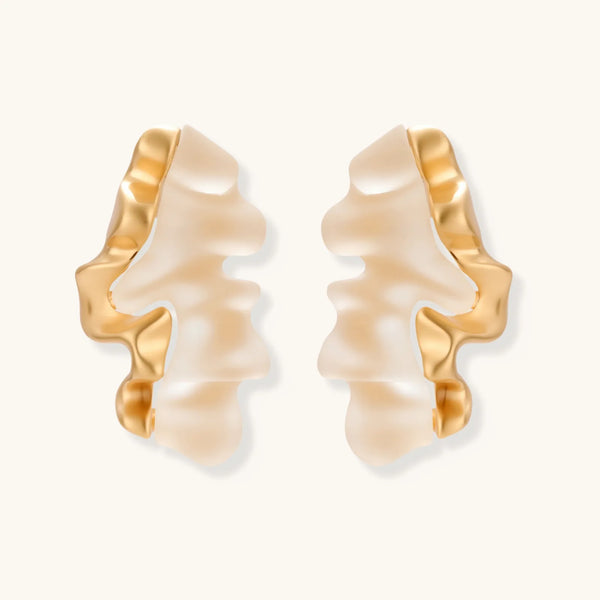 Sculptural wave-textured statement earrings with flowing organic ridges in metallic finish on cream background