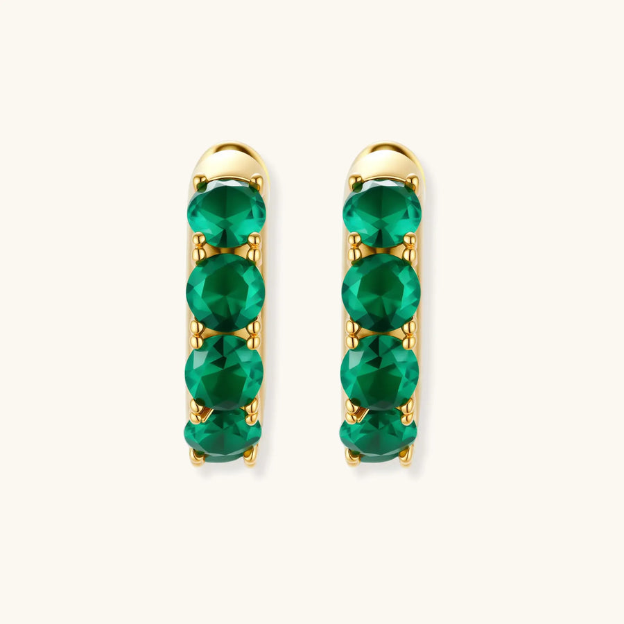 Close-up of gold-plated huggie hoop earrings featuring four emerald green cubic zirconia stones on white background.