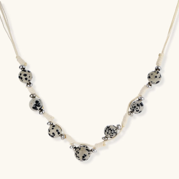 Adjustable cream cord necklace with white spotted stone beads featuring black speckles on neutral background