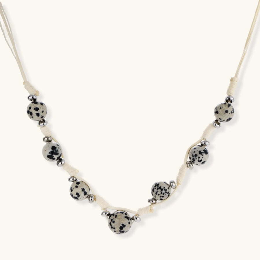 Adjustable cream cord necklace with white spotted stone beads featuring black speckles on neutral background