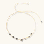 Adjustable cream cord necklace with white spotted stone beads featuring black speckles on neutral background