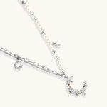 Silver-toned crescent moon pendant with star accents on pearl and chain necklace against white background.