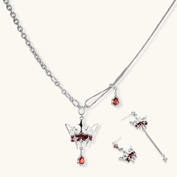 Silver-tone crown pendant with red zirconia stones and matching asymmetrical earrings on cream background