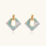 Geometric square enamel earrings with marbled turquoise and lavender pattern, gold U-shaped connector on cream background.