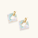Geometric square enamel earrings with marbled turquoise and lavender pattern, gold U-shaped connector on cream background.