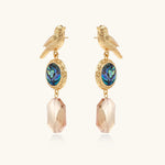 Gold-plated bird stud earrings with iridescent abalone shell medallions and champagne crystal drops on cream background