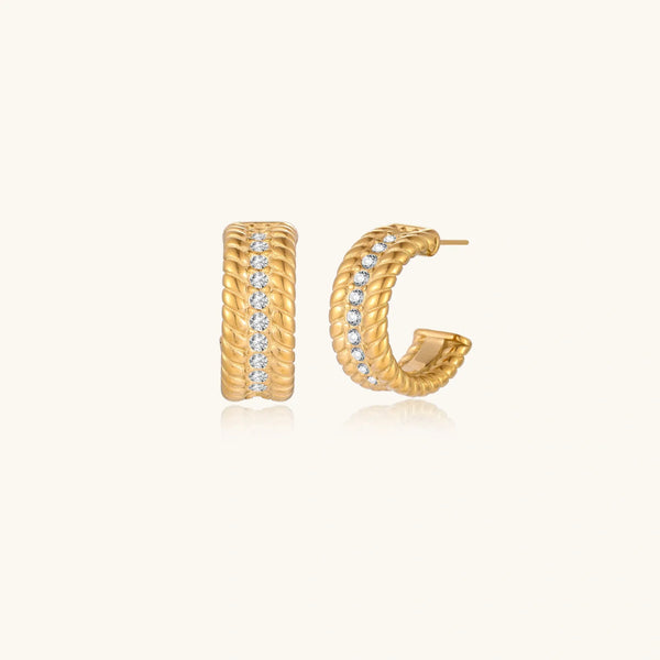 Textured gold huggie hoop earrings with raised ribbed rows creating dimensional sculptural design on cream background