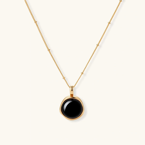 Circular black agate pendant on gold-plated sterling silver chain against cream background, showing modern minimalist design.