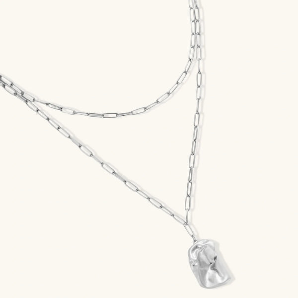Silver layered necklace with organic flowing pendant in eco-zinc alloy on neutral background, showing adjustable chain design.