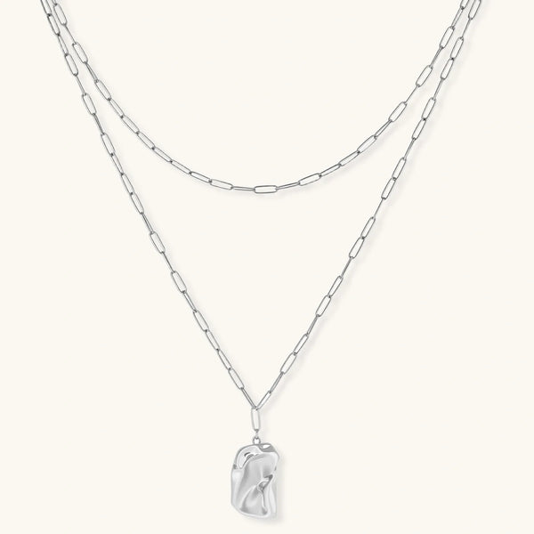 Silver layered necklace with organic flowing pendant in eco-zinc alloy on neutral background, showing adjustable chain design.