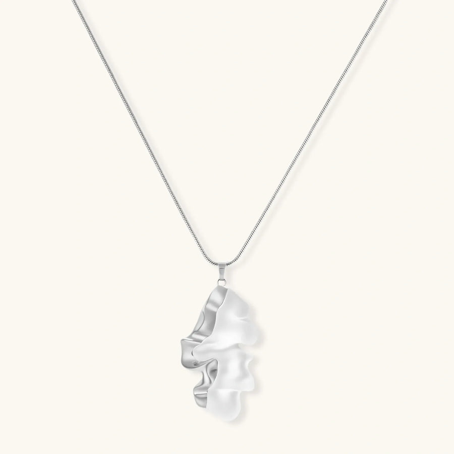 Modern sculptural pendant necklace with twisted metallic design on delicate silver chain against neutral background.