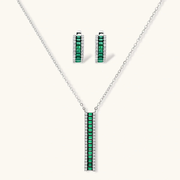 White gold plated jewelry set with emerald green rectangular stones and clear crystals in geometric rows on white background.