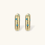 Gold-plated huggie hoop earrings with blue star inlays and textured surface, shown against white background.