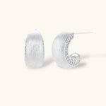 Close-up of small silver-plated hoop earrings with brushed texture and a row of sparkling zircon crystals on white background