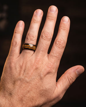 Harmonia men's black tungsten ring with whiskey barrel oak and guitar string inlay – worn on a man's hand